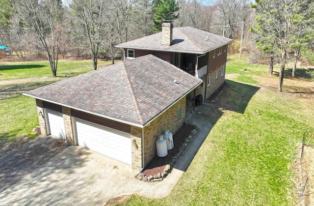 exterior space featuring roof with shingles, stone siding, a chimney, concrete driveway, and a lawn