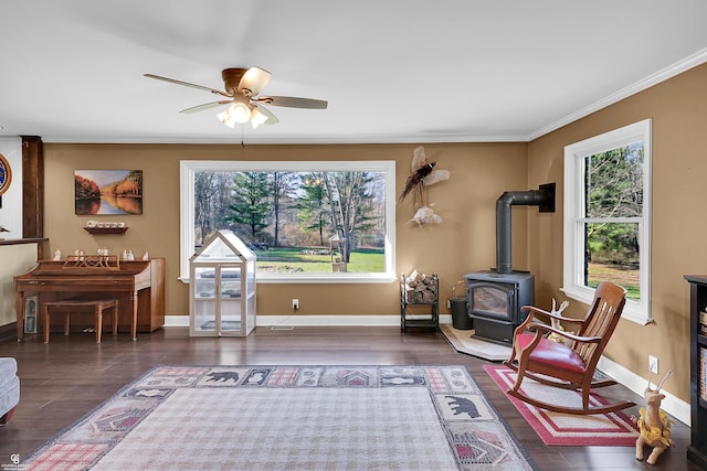 sitting room with wood finished floors, a wood stove, ornamental molding, and ceiling fan