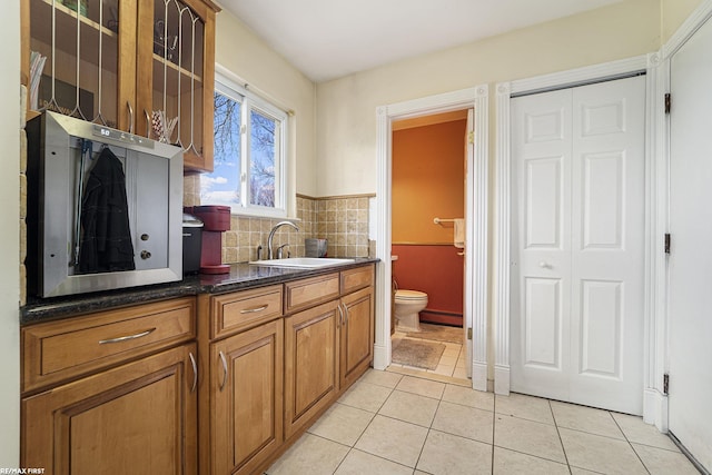 kitchen featuring glass insert cabinets, light tile patterned flooring, brown cabinets, a baseboard radiator, and a sink