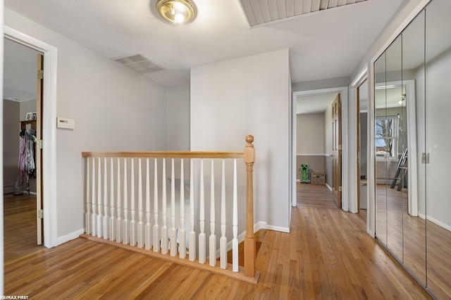hallway featuring baseboards, wood finished floors, and an upstairs landing