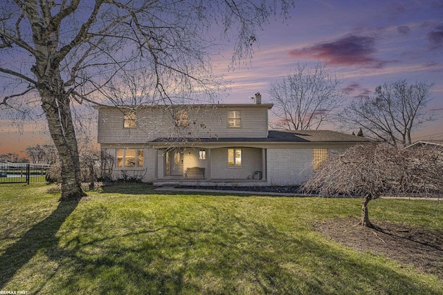 view of front of property with brick siding, a chimney, fence, and a lawn