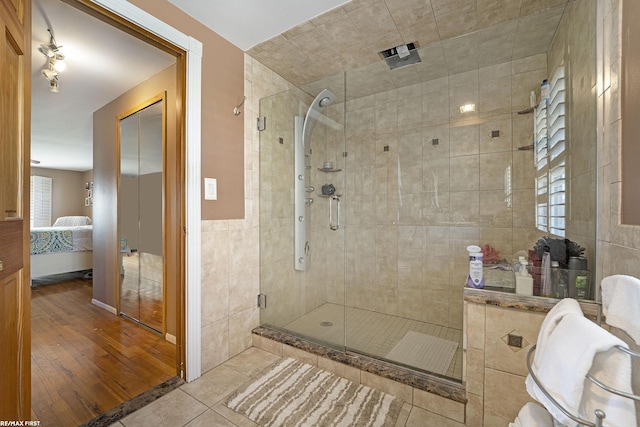 ensuite bathroom with a shower stall, ensuite bath, tile patterned flooring, and tile walls