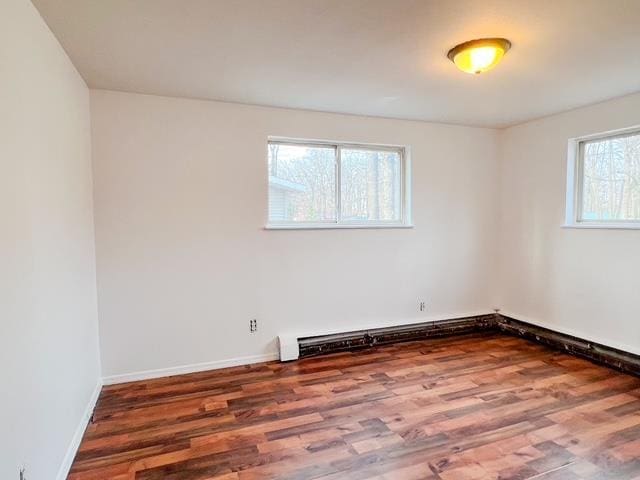 spare room featuring a baseboard heating unit, wood finished floors, and baseboards