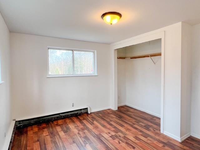 unfurnished bedroom with baseboards, wood finished floors, a closet, and a baseboard radiator
