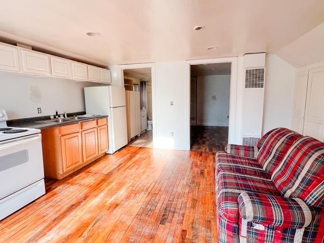 kitchen with dark countertops, light wood finished floors, a sink, and white appliances