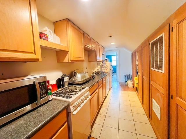 kitchen featuring white range with gas cooktop, dark countertops, stainless steel microwave, and light tile patterned flooring