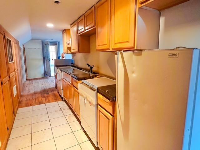 kitchen with dark countertops, a sink, light tile patterned floors, lofted ceiling, and freestanding refrigerator