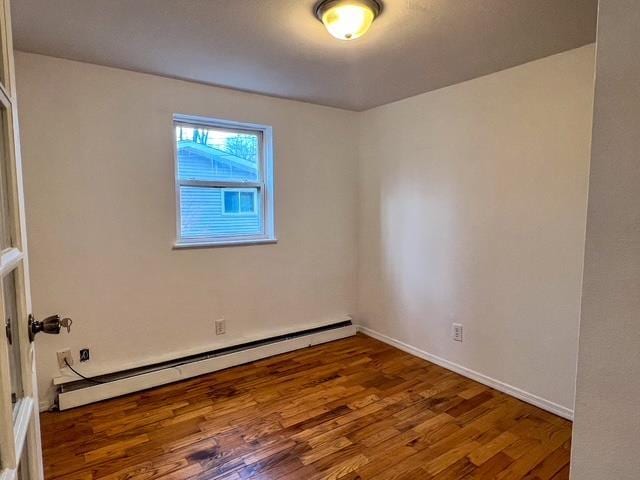unfurnished room with a baseboard heating unit, baseboards, and wood finished floors