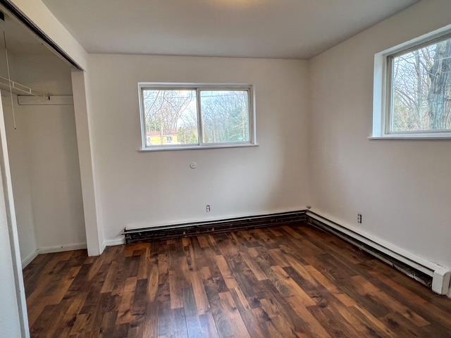 unfurnished bedroom featuring a baseboard heating unit, wood finished floors, a closet, and baseboard heating