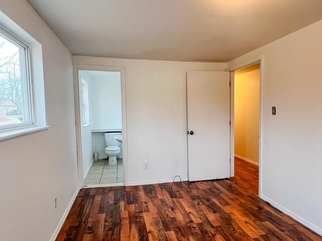 unfurnished bedroom with ensuite bath, baseboards, and wood finished floors