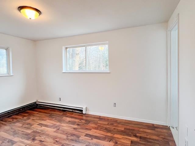empty room featuring a baseboard heating unit, baseboards, and wood finished floors