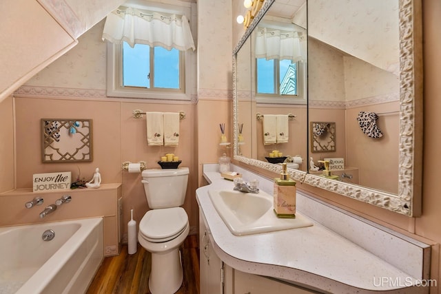 full bathroom with a bath, toilet, wallpapered walls, wood finished floors, and vanity