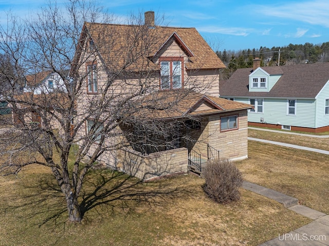 view of front facade featuring a chimney, a shingled roof, and a front yard