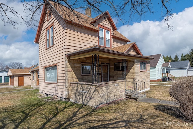 view of front of house with roof with shingles, a porch, a front yard, and a chimney