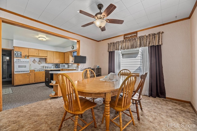dining room featuring a ceiling fan, baseboards, light colored carpet, and crown molding
