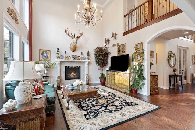living room featuring a towering ceiling, an inviting chandelier, wood finished floors, arched walkways, and a fireplace