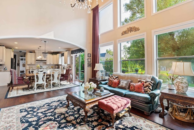 living room featuring arched walkways, dark wood-style flooring, a chandelier, and a towering ceiling