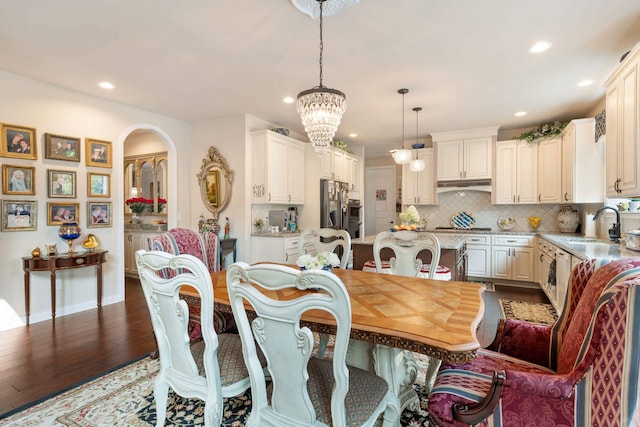 dining area with arched walkways, dark wood finished floors, an inviting chandelier, and recessed lighting