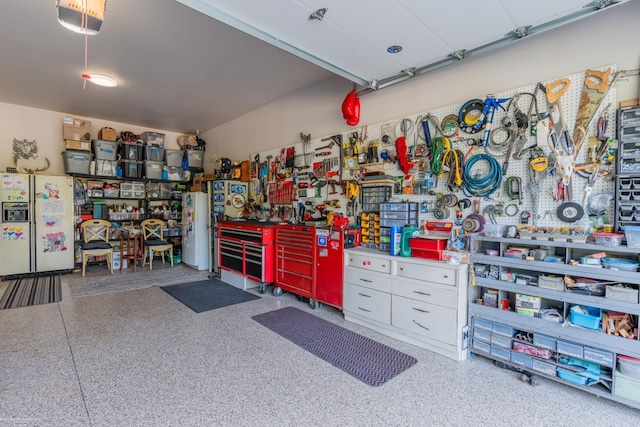 garage with a workshop area, white fridge with ice dispenser, and freestanding refrigerator