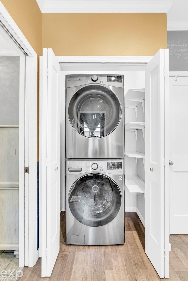 clothes washing area featuring wood finished floors, stacked washer and clothes dryer, laundry area, and ornamental molding