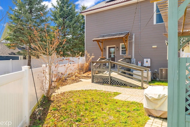 back of house featuring a fenced backyard, central air condition unit, a wooden deck, a patio, and a lawn