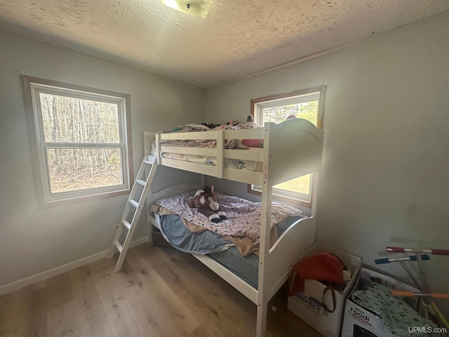 bedroom featuring baseboards, wood finished floors, and a textured ceiling