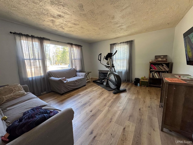 exercise area with a textured ceiling, a healthy amount of sunlight, and light wood finished floors
