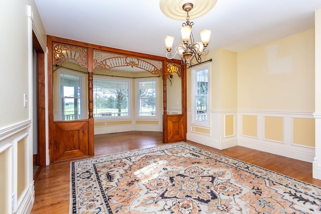 interior space with wood finished floors, a decorative wall, a wainscoted wall, and a notable chandelier