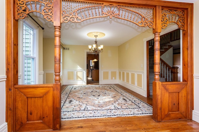 foyer with wood finished floors, visible vents, a decorative wall, wainscoting, and a notable chandelier