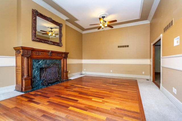unfurnished living room with visible vents, a high end fireplace, wood finished floors, ceiling fan, and ornamental molding