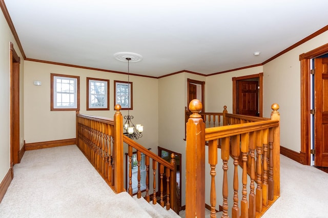 hallway featuring baseboards, a notable chandelier, an upstairs landing, carpet floors, and ornamental molding