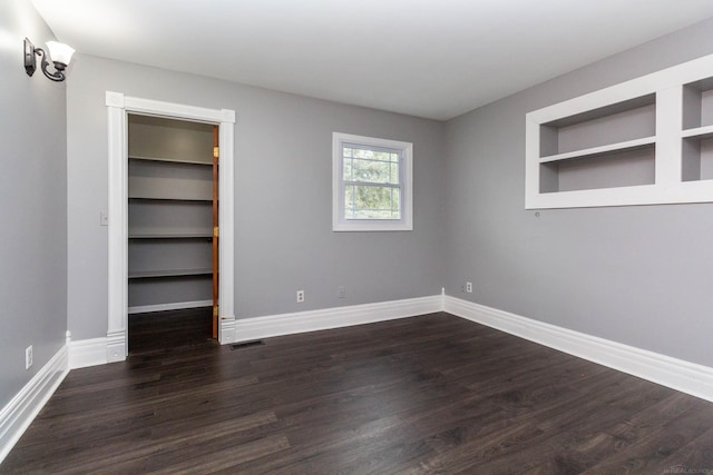 unfurnished bedroom with a walk in closet, baseboards, visible vents, and dark wood-type flooring