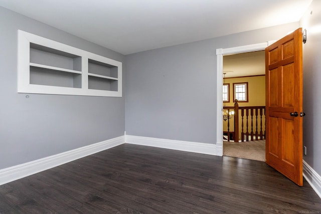 empty room featuring baseboards, dark wood-style floors, and built in features