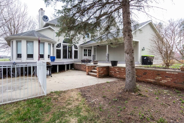 back of property featuring a chimney, a sunroom, a patio, and a shingled roof