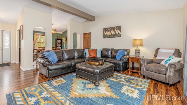 living area featuring baseboards, vaulted ceiling with beams, wood finished floors, and arched walkways