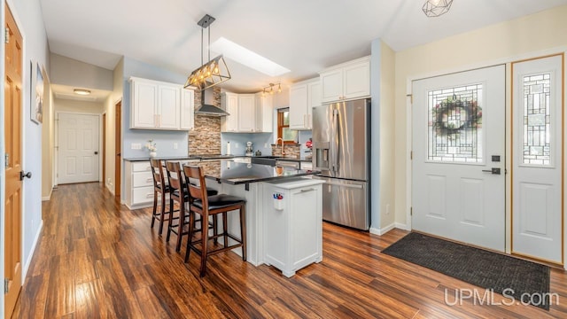 kitchen with white cabinets, dark countertops, stainless steel fridge with ice dispenser, a kitchen island, and dark wood-type flooring