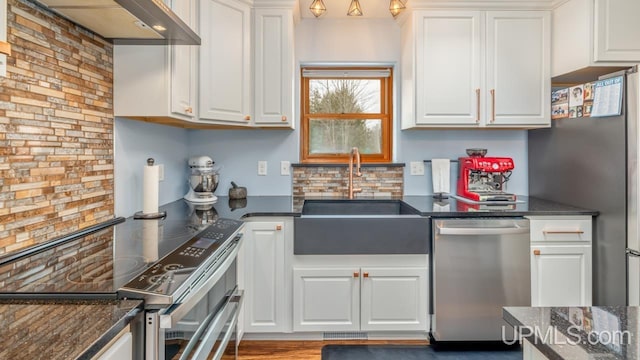 kitchen featuring white cabinets, appliances with stainless steel finishes, wall chimney range hood, and a sink
