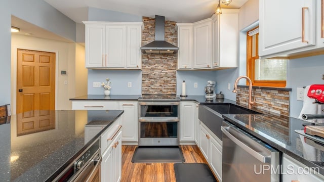 kitchen with wall chimney exhaust hood, white cabinetry, stainless steel appliances, and a sink