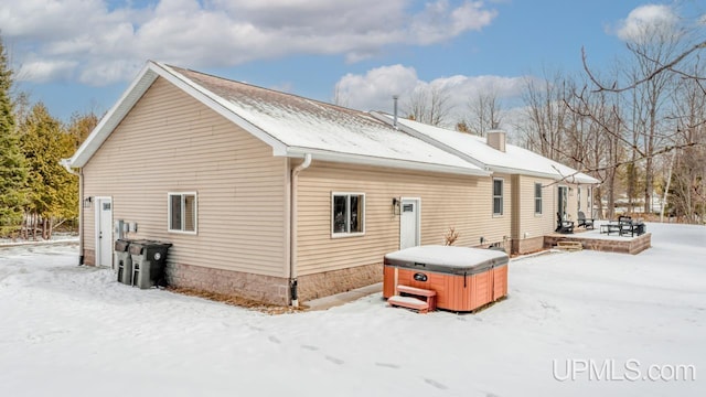 snow covered property with a chimney, a hot tub, and a patio