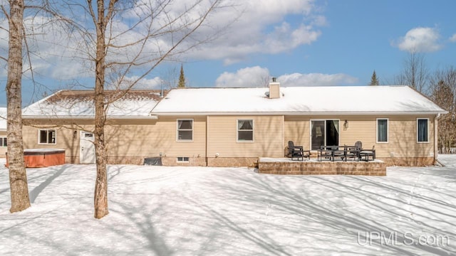 snow covered house with a chimney, a hot tub, and a patio area