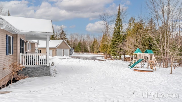 yard layered in snow with a detached garage and a playground