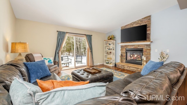 living room featuring a stone fireplace, vaulted ceiling, wood finished floors, and baseboards