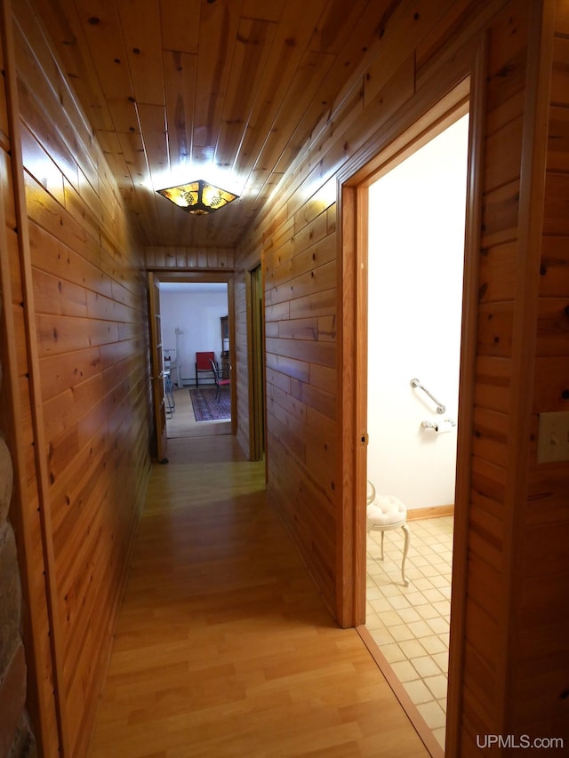 corridor with light wood-style flooring, wood walls, and wooden ceiling