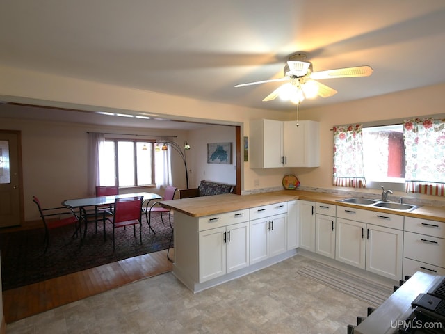 kitchen with ceiling fan, a peninsula, white cabinetry, and a sink