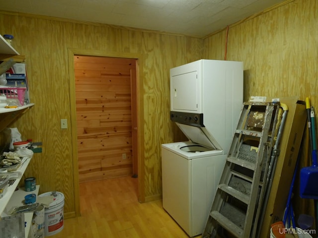 clothes washing area with wooden walls, light wood-type flooring, stacked washer / dryer, and laundry area