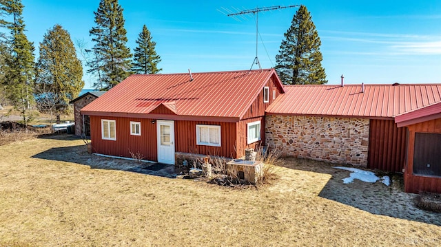 rear view of house featuring stone siding, a yard, and metal roof