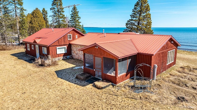 exterior space with a sunroom, stone siding, a water view, and metal roof