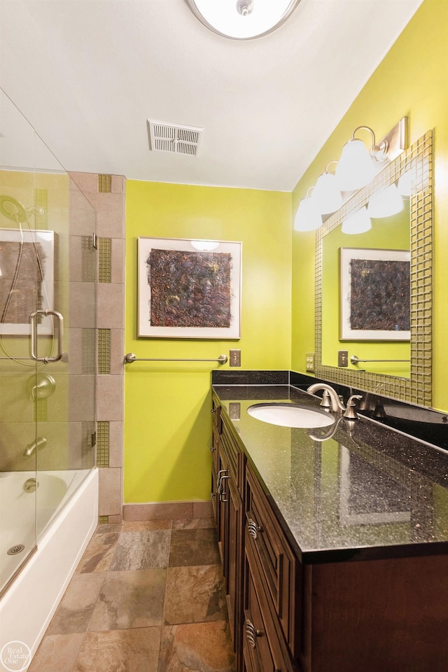 full bath with vanity, enclosed tub / shower combo, baseboards, stone finish floor, and visible vents
