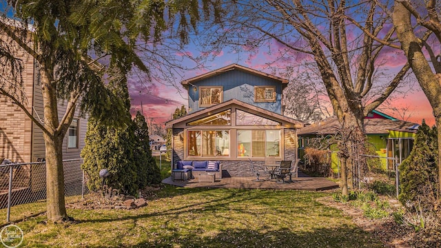 back of house at dusk with an outdoor hangout area, a lawn, stone siding, and fence