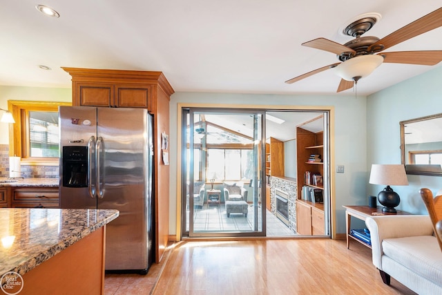 kitchen with light stone countertops, a healthy amount of sunlight, brown cabinets, and stainless steel fridge with ice dispenser